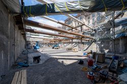 Baustelle mit mehreren Rohrebenen, Aushub, Baumaschinen, Gerüsten und einem städtischen Gebäude.