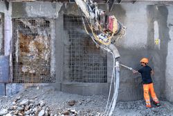 Bauarbeiter trägt Spritzbeton mit einem mechanischen Arm und einer Düse auf eine drahtbewehrte Wand auf einer Baustelle auf.